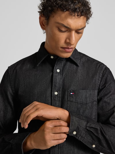 Männermodel trägt Regular Fit Jeanshemd aus reiner Baumwolle von Tommy Hilfiger in Black Denim mit Kentkragen, Nahaufnahme Oberkörper.