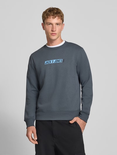Männermodel trägt Regular Fit Sweatshirt mit Baumwoll-Anteil Modell 'Munk' von JACK & JONES, dunkler Farbton, Logo-Print, Nahaufnahme Oberkörper.