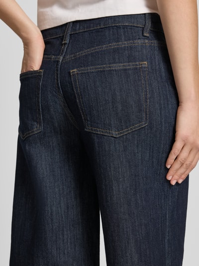 Kobiece modelka nosi Long Shorts mit Eingrifftaschen od Gina Tricot z mieszanki bawełny z dodatkiem streczu, krój loose fit, widoczne wpuszczane kieszenie i kieszenie z tyłu, zapięcie na guzik i zamek błyskawiczny, szerokość w rozmiarze 36: 42 cm, długość wewnętrzna nogawki w rozmiarze 36: 31 cm, ciemnoniebieska tkanina dżinsowa, zbliżenie na tylną część.