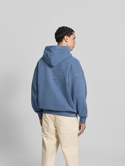 Männermodel trägt Oversized Sweatjacke aus Baumwolle von ANNARR in Blau mit Zweiwege-Reißverschluss, elastischen Abschlüssen, Balloon-Look, Ganzkörperansicht Rückansicht.