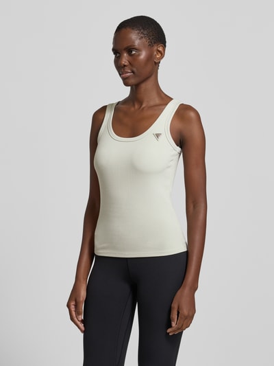 Frauenmodel trägt Slim Fit Top aus Viskose-Mix Modell 'Colette' von Guess Activewear in Hellbeige mit Logo, Rundhalsausschnitt, Nahaufnahme Oberkörper.