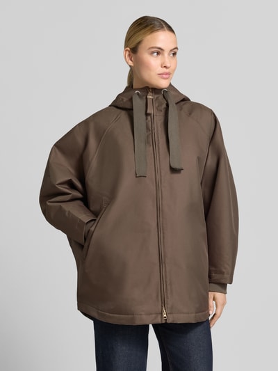 Frauenmodel trägt Relaxed Fit Mantel mit Kapuze Modell 'PURE' von g-lab in Braun, glatte Textur, Eingrifftaschen, Nahaufnahme Oberkörper.