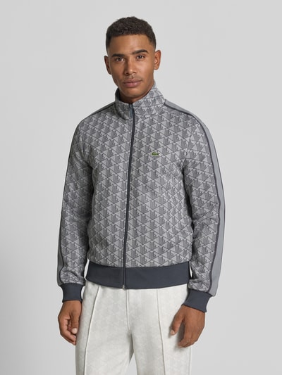 Männermodel trägt Regular Fit Sweatjacke mit Reißverschluss von Lacoste in Grau mit geometrischem Muster, Ganzkörperansicht von vorne.