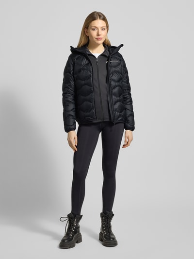 Frauenmodel trägt Steppjacke mit Daunen-Federn-Füllung Modell 'Helium' von PEAK PERFORMANCE, schwarze Farbe, glatte Textur, Ganzkörperansicht von vorne, Regular Fit, Kapuze, Reißverschluss, Label-Stitching, Rückenlänge 62 cm, Schulterbreite 42 cm, Brustweite 50 cm, Ärmellänge 63 cm.