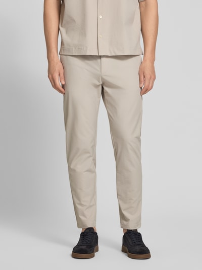 Männermodel trägt Tapered Chino mit Tunnelzug von BOSS Orange in Beige, unifarben, mit Gürtelschlaufen und Eingrifftaschen, Ganzkörperansicht von vorne.