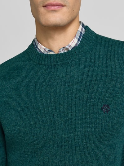 Männermodel trägt Slim Fit Strickpullover aus reiner Wolle mit Label-Stitching von MCNEAL, grün, gerippte Abschlüsse, Nahaufnahme Oberkörper.