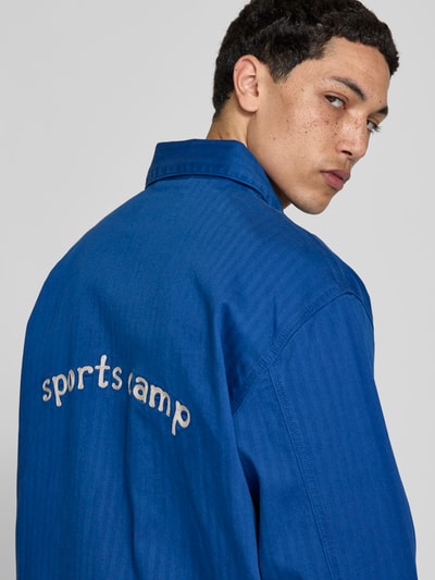 Männermodel trägt Hemdjacke mit Motiv-Stitching von Forét in Blau, Baumwoll-Mix, Relaxed-Fit, Rückenlänge 73 cm, Nahaufnahme Rückansicht.