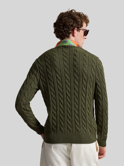 Męski model nosi Regular Fit Strickpullover aus reiner Baumwolle od Polo Ralph Lauren w jednolitym oliwkowym kolorze, wzór warkoczowy, długie rękawy, cienka dzianina, okrągły dekolt, dzianinowe ściągacze, widoczne logo, krój regular fit, widok całej sylwetki od tyłu.