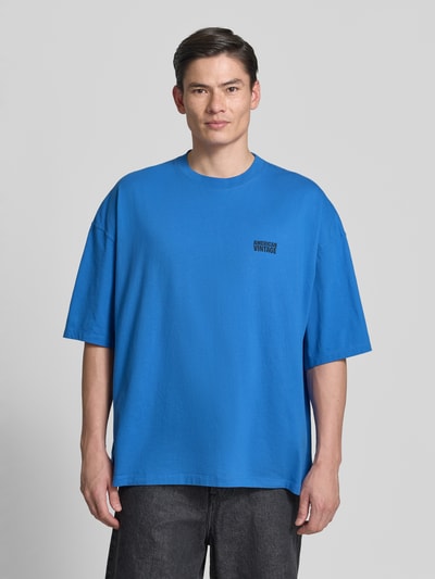 Männermodel trägt Herren T-Shirt mit Logo-Print, Modell 'GIXY' von American Vintage, kräftiges Blau, Reine Baumwolle, Loose-Fit, Rundhalsausschnitt, überschnittene Schultern, Rückenlänge bei Größe M/L: 72 cm, Ganzkörperansicht von vorne.