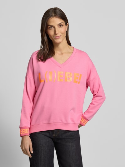 Frauenmodel trägt Oversized Sweatshirt mit Statement-Print von miss goodlife in Pink, reine Baumwolle, V-Ausschnitt, Ganzkörperansicht von vorne.