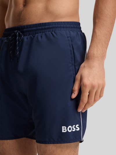 Männermodel trägt dunkelblaue Badeshorts mit Kontrast-Logo Modell 'STARFISH' von BOSS, Kontrastnaht, Nahaufnahme Oberschenkel.