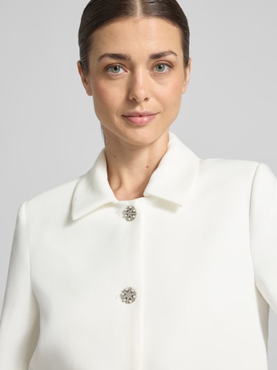 Frauenmodel trägt Blazer mit Viskose-Anteil Modell 'Leonie' von GUIDO MARIA KRETSCHMER WOMAN, weiße Farbe, Nahaufnahme Oberkörper. Elastischer-Material-Mix, Regular-Fit, Umlegekragen, durchgehende Knopfleiste mit Perlenbesatz, Paspeltaschen, Rückenlänge bei Größe 36: 48 cm.