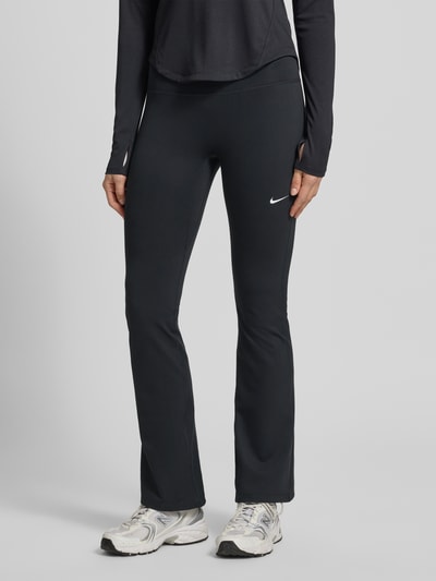 Frauenmodel trägt Flared Cut Leggings mit Logo von NIKE TRAINING aus schwarzem Material-Mix mit Stretch-Anteil, elastischer Bund, Logo, Nahaufnahme Unterkörper.