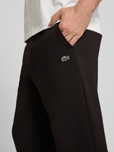 Mężczyzna nosi Regular Fit Sweatpants aus Baumwoll-Mix von Lacoste, efekt: jednolity kolor, wyhaftowane logo, mieszanka bawełny, dzianina dresowa, wpuszczane kieszenie, wykończenie: elastyczny ściągacz, zapięcie: tunel, detal: polar szczotkowany, zbliżenie na kieszeń z przodu
