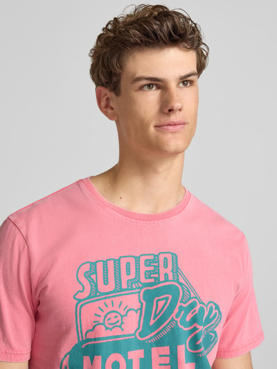 Männermodel trägt Loose Fit T-Shirt mit Label-Print Modell 'Roadside Trade' von Superdry aus Reine Baumwolle in Rosa, Nahaufnahme Oberkörper.