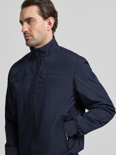 Männermodel trägt Regular Fit Jacke mit Stehkragen Modell 'Finlay' von SAVE THE DUCK, Zweiwegereißverschluss, elastische Abschlüsse, marineblau, Nahaufnahme Oberkörper.