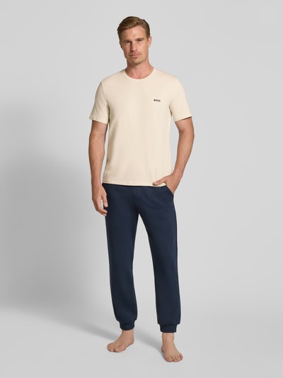 Männermodel trägt Regular Fit T-Shirt aus Baumwoll-Mix von BOSS in Beige und dunkelblaue Hose, Ganzkörperansicht von vorne. Herren T-Shirt von BOSS