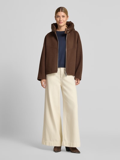 Frauenmodel trägt Doubleface Wolljacke mit abnehmbarer Steppkapuze von Blonde No. 8 in Braun, entspannter Schnitt, Ganzkörperansicht von vorne. Wollmischung, Zweiwege-Reißverschluss, elastische Ärmelabschlüsse, mittlere Rückenlänge, betonte Schulter, großzügige Brustweite, lange Ärmel.