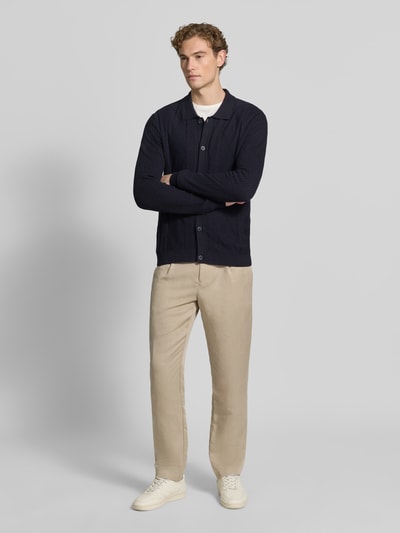 Männermodel trägt Strickjacke mit Strukturmuster Modell 'YARO' von CINQUE in Dunkelblau, Slim Fit, Knopfleiste, Beige Hose, Ganzkörperansicht von vorne.