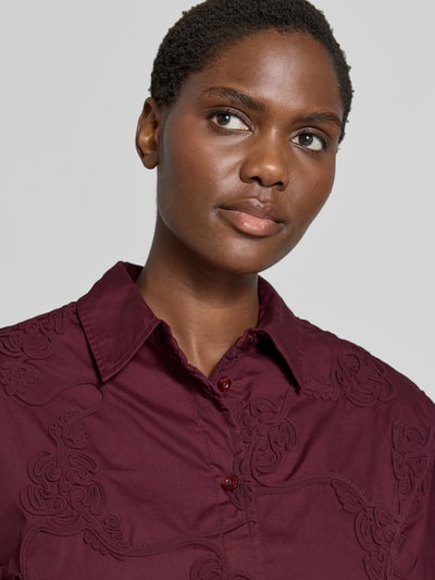 Frauenmodel trägt Oversized Hemdbluse aus reiner Baumwolle von ROTATE in Dunkelrot mit floralen Stickereien, Nahaufnahme Oberkörper.