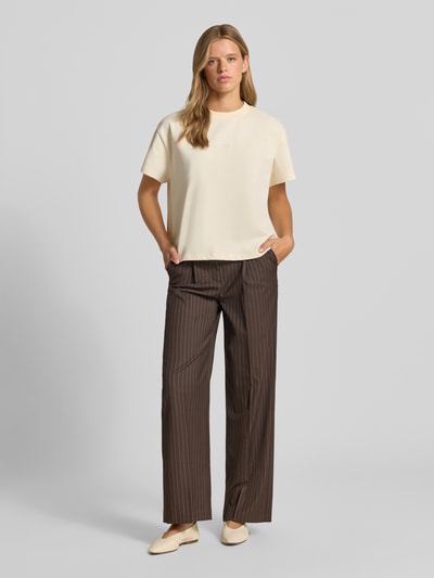 Frauenmodel trägt T-Shirt mit Logo-Stitching Modell 'Ella' von OH APRIL in Creme, Boxy Fit, Rundhalsausschnitt, Baumwolle, Ganzkörperansicht von vorne.