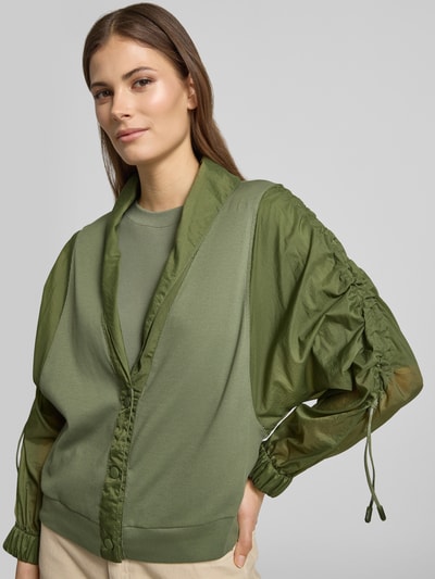 Modelka kobieca nosi Relaxed Fit Leichte Jacke im Material-Mix von Marc Cain, efekt: jednolity kolor, krój relaxed fit, krótki szalowy kołnierz, marszczenie, zapięcie na ukryte guziki, rękaw o dł. 3/4, wykończenie materiału: satyna, szyfon, materiał: mieszanka bawełny, kolor zielony, kształty miękkie, tekstura gładka z półprzezroczystymi rękawami, ujęcie: z przodu, od pasa w górę