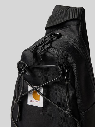 Produktfoto, Sling Bag mit Logo-Patch Modell 'Kyle' von Carhartt Work In Progress in Schwarz, Reißverschluss, Tunnelzug, robuste Textur, Detailaufnahme, Hauptfach, verstellbarer Schulterriemen, Maße 20x35x10 cm, Riemenlänge 90 cm