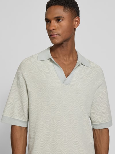Mężczyzna nosi Relaxed Fit Poloshirt mit V-Ausschnitt Modell 'LAURENZZO' von Drykorn, mieszanka bawełny, jasne kolory, wzór allover, szczegóły kołnierzyka, długość tyłu w rozmiarze M: 67 cm, zbliżenie górnej części ciała z przodu.