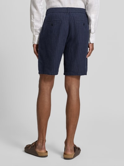 Männermodel trägt Straight Fit Leinenshorts mit Gesäßtaschen von Gant aus Reine Leinen, dunkelblau mit feinen Streifen, Ganzkörperansicht Rückansicht.