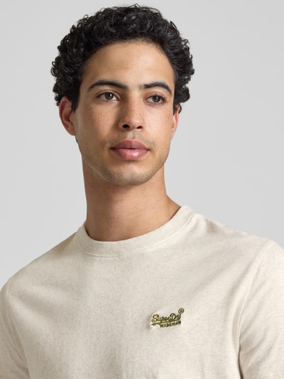 Männermodel trägt Regular Fit T-Shirt mit Logo-Stitching von Superdry in Beige, reine Baumwolle, Rundhalsausschnitt, Nahaufnahme Oberkörper.