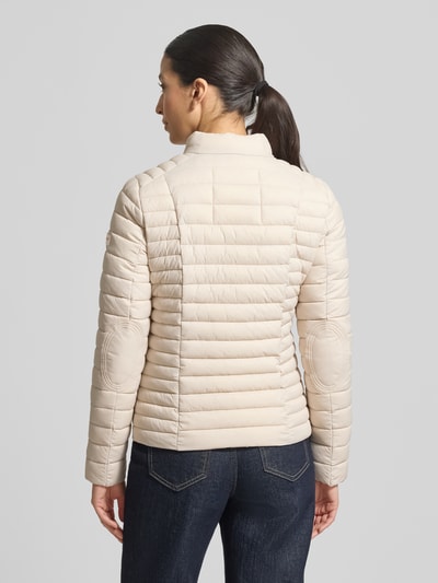 Vrouwenmodel draagt gewatteerd jack met opstaande kraag Model 'JUDY' van Frieda & Freddies, slim fit, ruglengte 57 cm, schouderbreedte 40 cm, borstwijdte 48 cm, mouwlengte 64 cm, tweewegritssluiting, ritszakken, geheel beige, rechte lijnen structuur, gladde textuur, geheel zichtbare rug, rugaanzicht.
