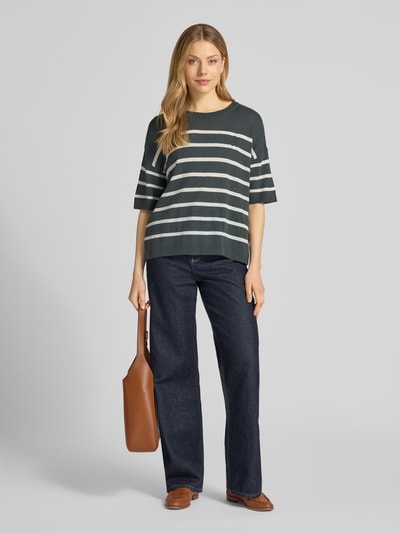Frauenmodel trägt Relaxed Fit Pullover aus Leinen-Mix Modell 'STRIPE' von Armedangels mit Allover-Muster, Streifen-Design in dunklem Grün mit weißen Streifen, Rundhals, 1/2-Arm, Strick, gerippte Abschlüsse, Logo-Stitching, Materialverarbeitung: Strick, Ganzkörperansicht von vorne.