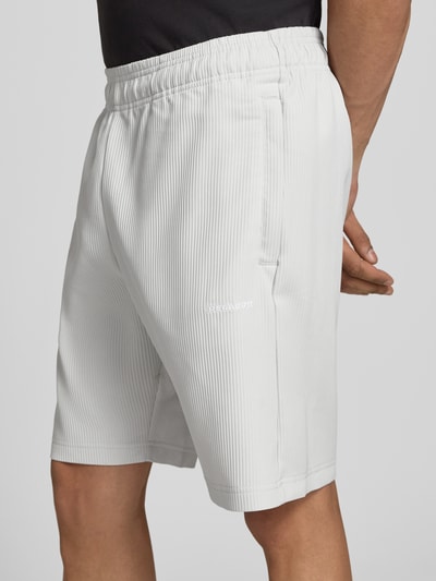 Männermodel trägt Shorts mit Logo Modell 'Troy' von Pegador aus weißem Material-Mix mit Stretch-Anteil, elastischer Bund, Nahaufnahme Oberschenkel.