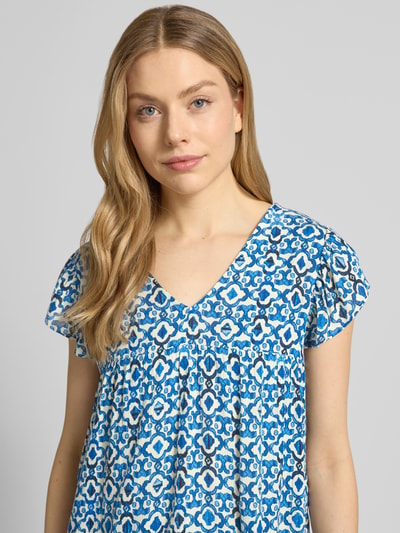 Kobiece modelka nosi Blusenshirt aus Viskose Modell 'MARRAKECH' od ICHI, wzór na całej powierzchni, dekolt w serek, krój regular fit, długość tyłu w rozmiarze S: 54 cm, niebiesko-biały, faktura miękka, zbliżenie na górną część ciała