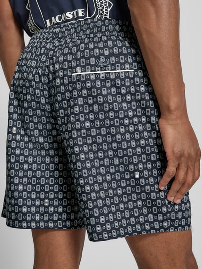 Mężczyznamodel nosi Regular Fit Chinoshorts aus Baumwoll-Viskose-Mix Modell 'Aop Short Tenniscourt' von Lacoste, granatowe z białym wzorem, tekstura gładka, Herren Chinoshorts von Lacoste, Ganzkörperansicht Rückansicht.