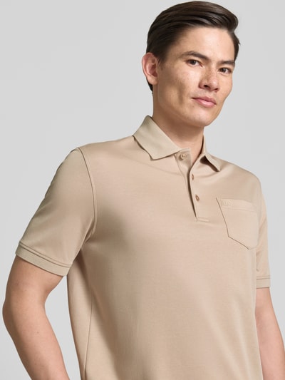Männermodel trägt Regular Fit Poloshirt mit Brusttasche und Label-Stitching von bugatti in Beige mit Polokragen und Knopfleiste, Nahaufnahme Oberkörper. Rückenlänge bei Größe M: 70 cm.