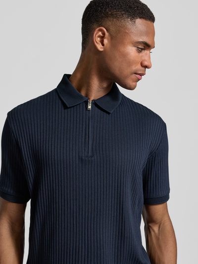 Männermodel trägt Regular Fit Poloshirt mit Baumwoll-Anteil Modell 'FAVE' von SELECTED HOMME in Dunkelblau, Rippstruktur, Nahaufnahme Oberkörper.