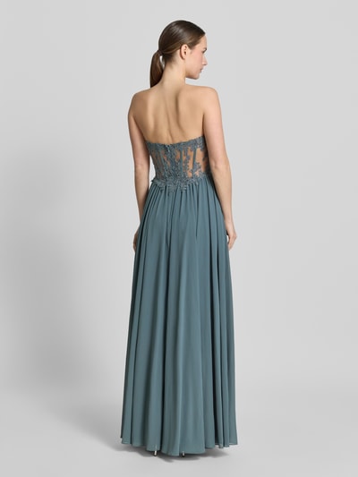 Frauenmodel trägt Abendkleid mit Spitze und Gehschlitz von Mascara in Blau, taillierter Schnitt, semitransparent, Rückansicht Ganzkörperansicht.
