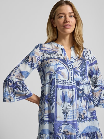Frauenmodel trägt Tunikakleid im Allover-Look mit V-Ausschnitt von Emily Van den Bergh in Blau mit grafischem Muster aus reiner Baumwolle, Trompetenärmel, A-Linie, Minikleid, Nahaufnahme Oberkörper.