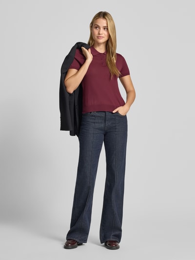 Frauenmodel trägt Poloshirt aus Viskose-Mix Modell 'LUXEN' von MANGO in Dunkelrot, kombiniert mit dunkler Hose, weiche Textur, Ganzkörperansicht von vorne. Taillierte Passform, Polokragen, gerippte Abschlüsse, Rückenlänge und Ärmellänge wie im Kontext beschrieben.