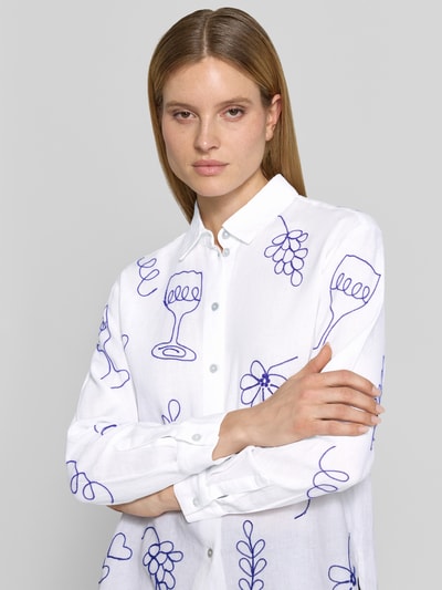 Frauenmodel trägt Regular Fit Leinenbluse im Allover-Look von Christian Berg Woman in Weiß mit blauen Motivstickereien, reine Leinen, Hemdblusenkragen, Knopfleiste, Nahaufnahme Oberkörper.