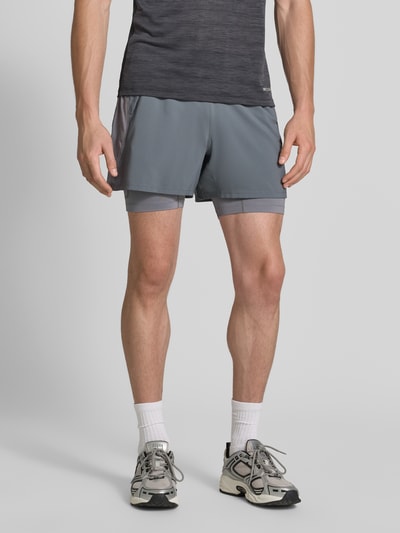Męski model nosi Regular Fit Shorts mit integrierten Tights Model 'Road' od ASICS TIGER, szarości, detal z logo, krój regular fit, elastyczny pas, Szerokość w rozmiarze M: 38 cm, Długość wewnętrzna nogawki w rozmiarze M: 12 cm, Ganzkörperansicht von vorne.