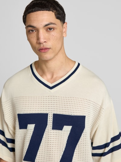 Männermodel trägt Strick-Trikot mit Jacquard Muster von REVIEW in Ecru mit navyblauen Streifen, perforowanie, dekolt w serek, rękaw o dł. 1/2, prosty krój, długość tyłu w rozmiarze M: 69 cm, trykotowy styl; Nahaufnahme Oberkörper