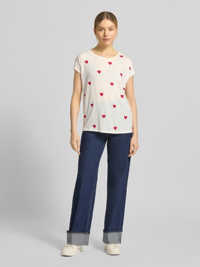 Frauenmodel trägt Relaxed Fit T-Shirt aus Lyocell-Mix Modell 'AVA' von Vero Moda, weiß mit rotem Allover-Herz-Print, kurzarm, Rundhals, Ganzkörperansicht von vorne.