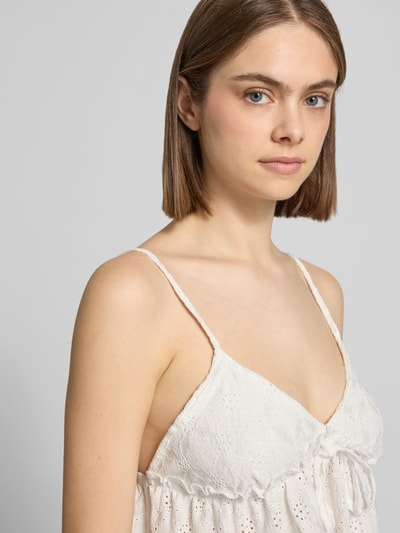 Kobiece modelka nosi Babydoll-Top mit Schößchendetail und Lochstickerei od REVIEW, mieszanka materiałów z dodatkiem streczu, krój regular fit, haft angielski, kolor biały, detal baskinka, długość tyłu w rozmiarze S: 27 cm, zbliżenie na górną część ciała z przodu
