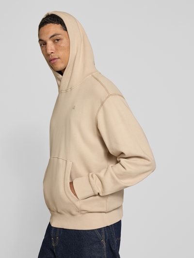 Männermodel trägt Regular Fit Hoodie aus reiner Baumwolle von G-Star RAW in Beige mit Kängurutasche, Ganzkörperansicht von vorne.