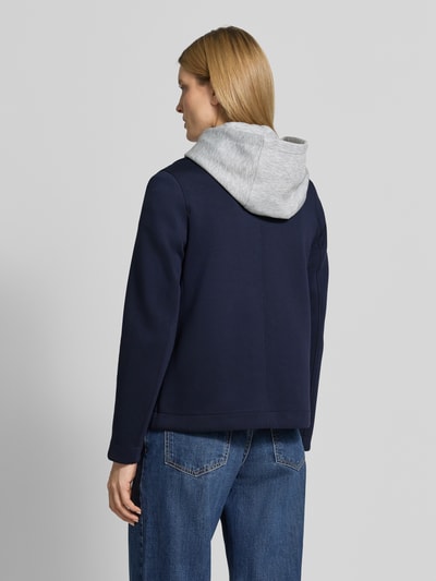 Modelka prezentuje Regular Fit Sweatjacke mit Viskose-Anteil od s.Oliver RED LABEL; granatowa, prosta forma, gładka faktura, tkanina dresowa, kaptur z dzianiny; krój regular fit, listwa guzikowa 2-rzędowa, wpuszczane kieszenie, widok całej sylwetki z tyłu.