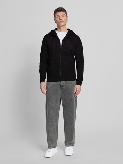 Mannmodel draagt Sweatjacke mit getrennter Kängurutasche van GAP in zwart, katoenmix, loose fit, label-stitching, elastische boorden, voorkant volledige lichaam.