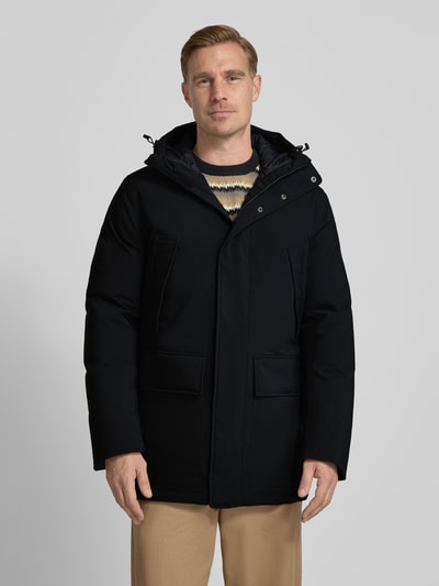Männermodel trägt Parka mit capuchon en klepzakken van PEAK PERFORMANCE, regular fit, ritssluiting, kleur donker, voorkant, Ganzkörperansicht von vorne. Ruglengte maat M 87 cm, schouderbreedte 47 cm, borstwijdte 59 cm, mouwlengte 73 cm.
