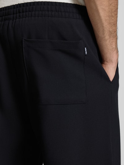 Männermodel trägt Straight Fit Stoffhose mit Viskose-Anteil von REVIEW in Schwarz, elastischer Bund, Gesäßtasche, Detailaufnahme Hüfte.